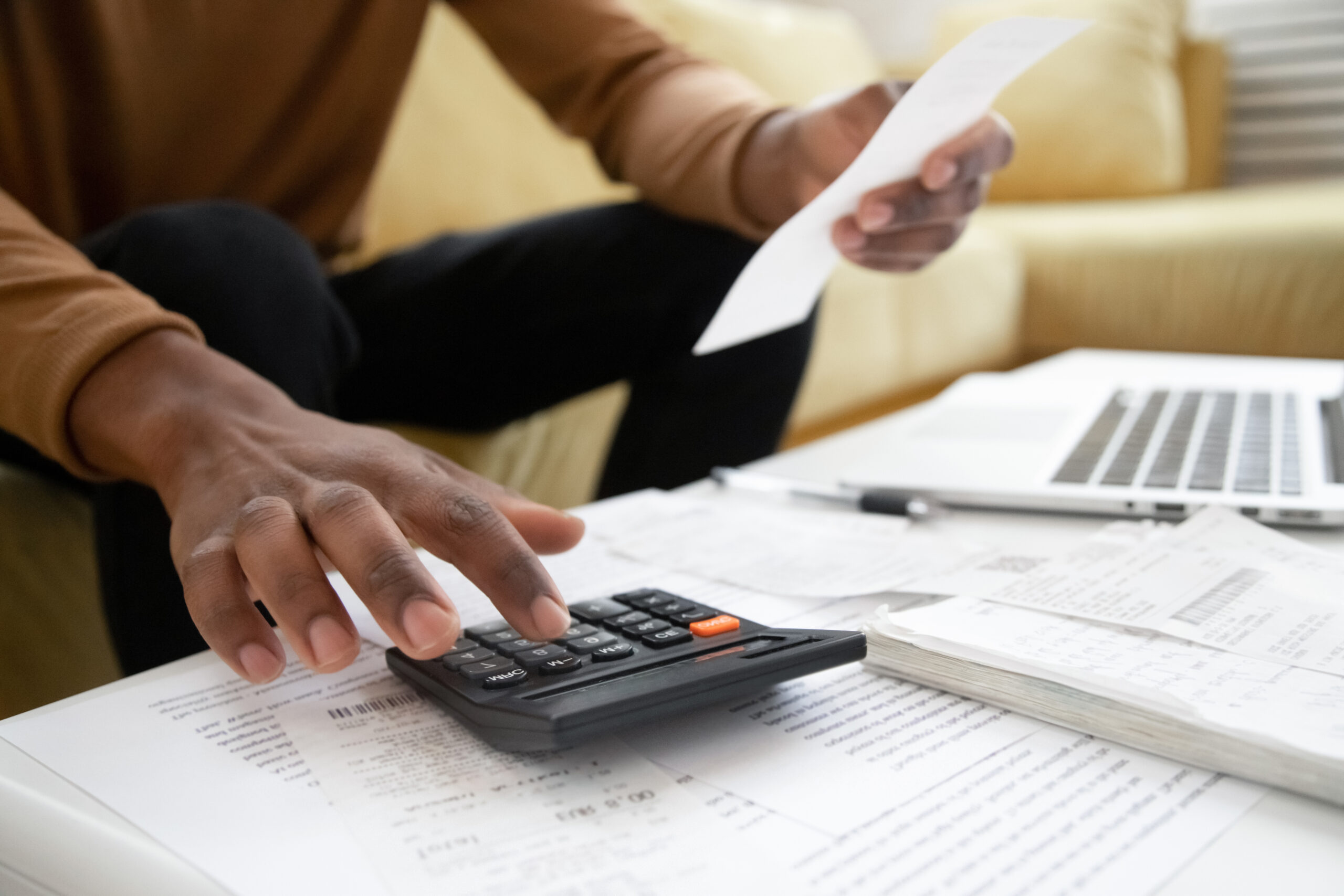 African American man using a calculator and laptop, while reviewing documents