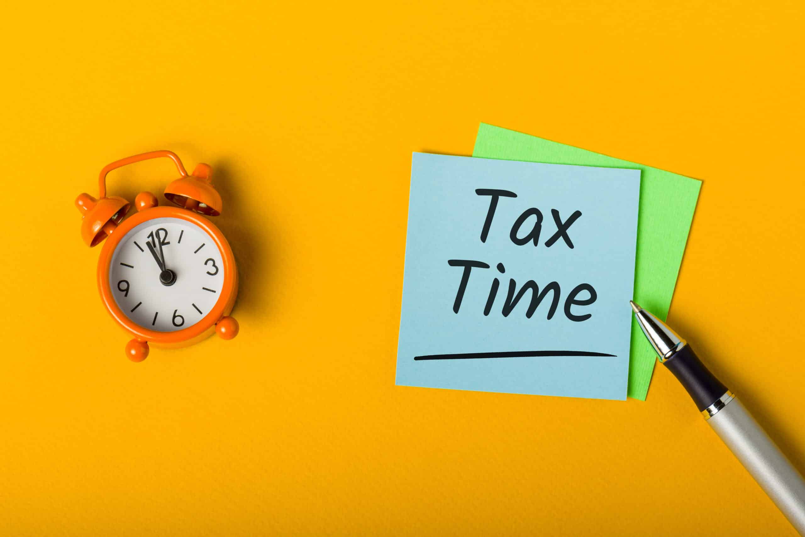 Orange background w alarm clock, a sticky note reading "tax time", and a pen.